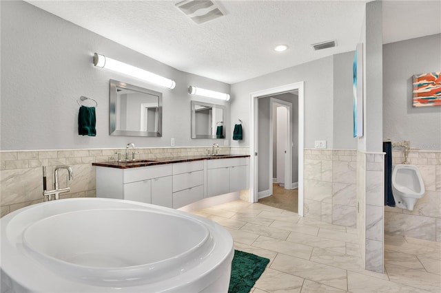 bathroom featuring vanity, a tub to relax in, a textured ceiling, and tile walls