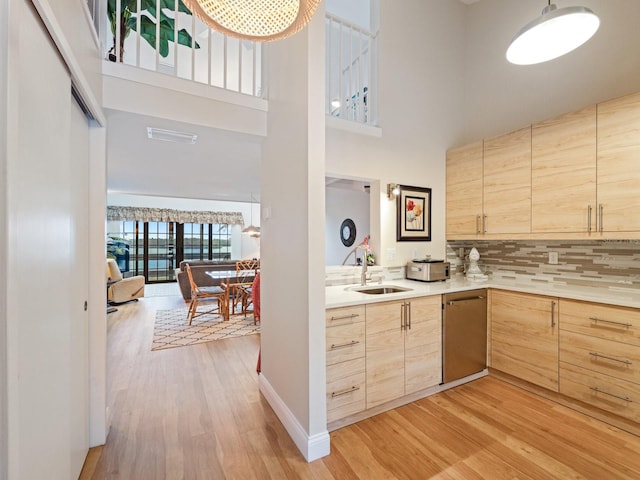 kitchen featuring sink, stainless steel dishwasher, a high ceiling, and light brown cabinets