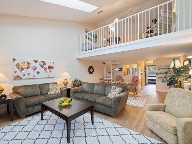 living room featuring light hardwood / wood-style floors, high vaulted ceiling, and a skylight