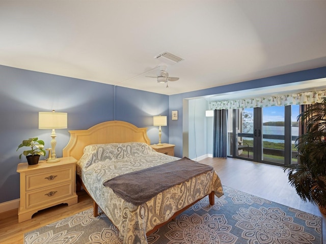 bedroom with access to outside, ceiling fan, light hardwood / wood-style floors, and a water view