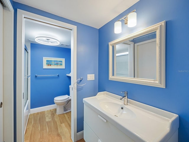 full bathroom with vanity, toilet, wood-type flooring, and bath / shower combo with glass door