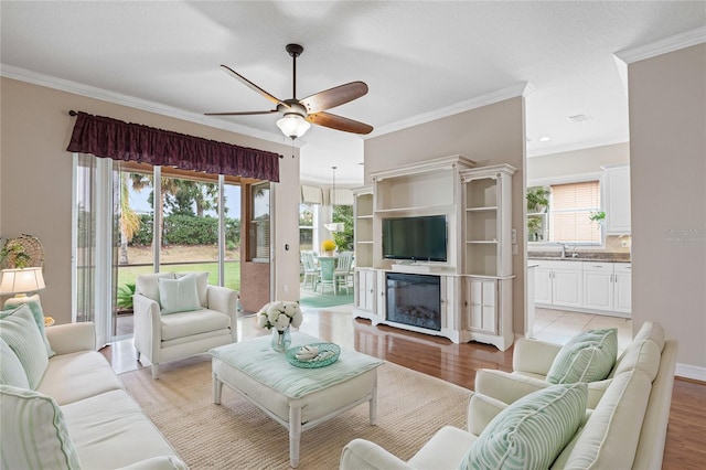 living room featuring light hardwood / wood-style flooring, a wealth of natural light, crown molding, and ceiling fan