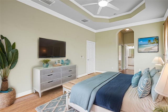 bedroom with ceiling fan, ensuite bathroom, crown molding, a tray ceiling, and light wood-type flooring