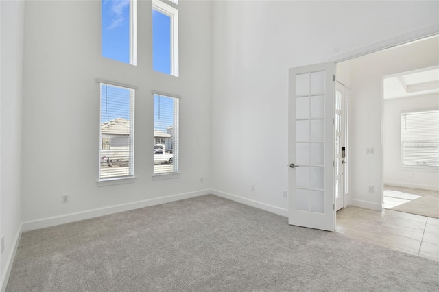 unfurnished room with a towering ceiling, light carpet, and french doors