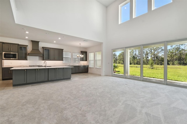 unfurnished living room with sink, light carpet, a high ceiling, and a chandelier