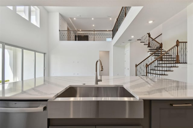 kitchen featuring light stone countertops, a high ceiling, dishwasher, and sink