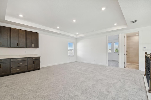 unfurnished living room featuring a tray ceiling, a wealth of natural light, and light colored carpet