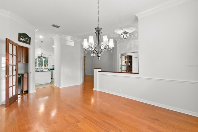 unfurnished dining area with light wood-type flooring, ornamental molding, french doors, and an inviting chandelier