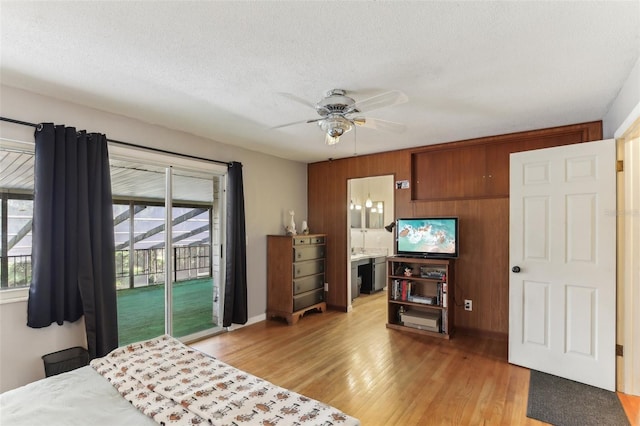 bedroom with ensuite bath, access to outside, ceiling fan, light hardwood / wood-style floors, and wood walls