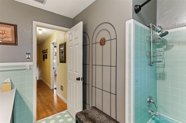 bathroom with tiled shower / bath combo, wood-type flooring, and tile walls