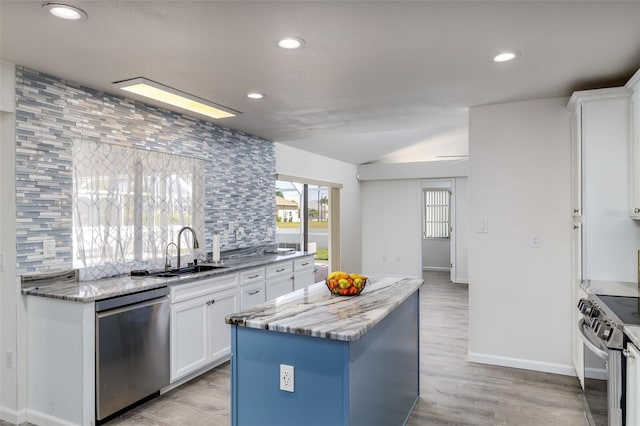 kitchen with light stone countertops, stainless steel appliances, a kitchen island, sink, and white cabinetry