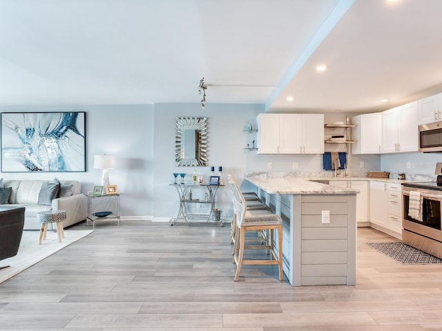 kitchen with white cabinets, light stone countertops, a kitchen bar, kitchen peninsula, and stainless steel appliances