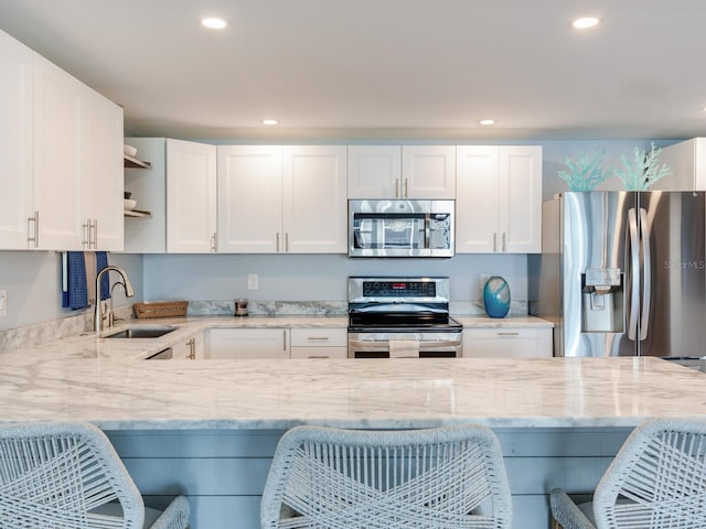 kitchen with light stone countertops, appliances with stainless steel finishes, a breakfast bar, sink, and white cabinetry