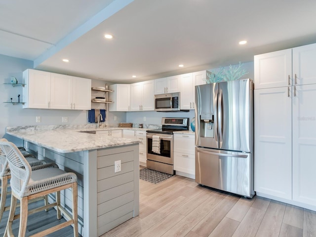 kitchen with kitchen peninsula, appliances with stainless steel finishes, a kitchen breakfast bar, white cabinets, and light hardwood / wood-style floors