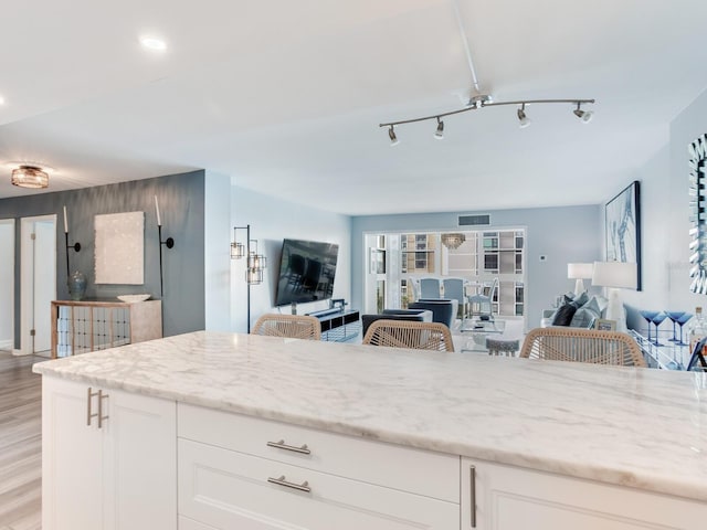 kitchen with white cabinets, light wood-type flooring, light stone countertops, and a breakfast bar area