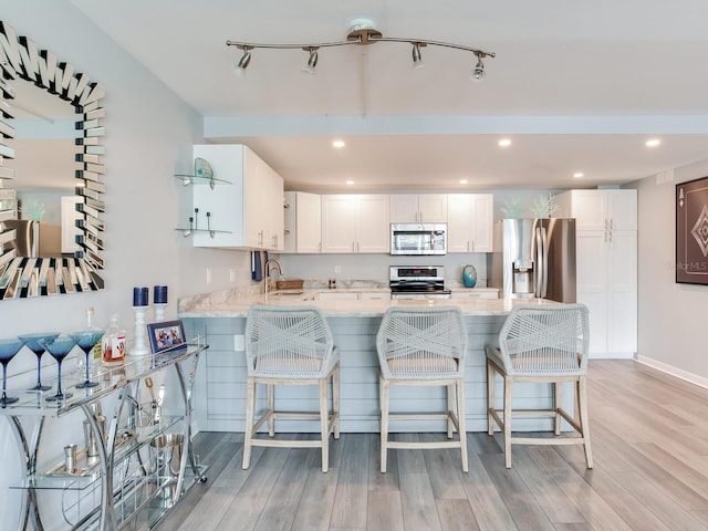 kitchen with white cabinets, light wood-type flooring, stainless steel appliances, and a breakfast bar area