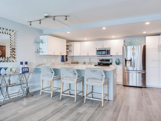 kitchen featuring a kitchen bar, kitchen peninsula, white cabinetry, and stainless steel appliances