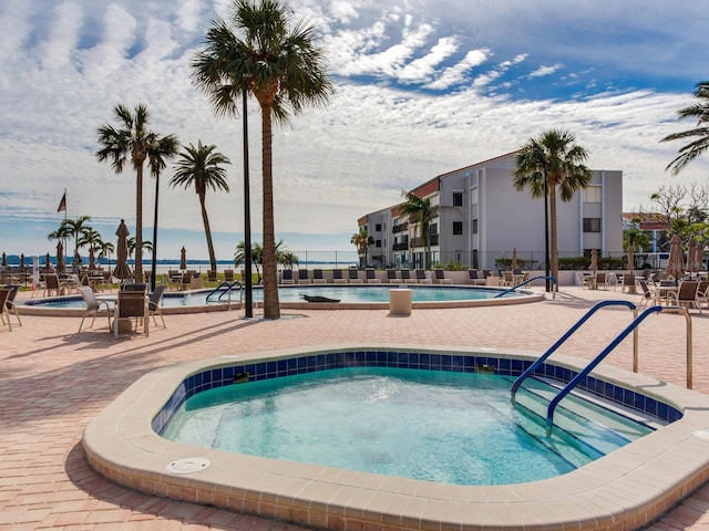 view of pool featuring a patio area, a water view, and a hot tub