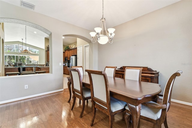 dining space with hardwood / wood-style flooring, lofted ceiling, and an inviting chandelier