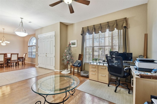 office area with ceiling fan with notable chandelier, light hardwood / wood-style floors, a textured ceiling, and a wealth of natural light