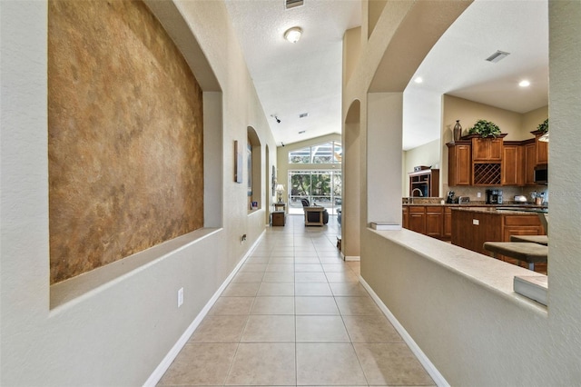 hallway featuring a textured ceiling, light tile patterned floors, and vaulted ceiling