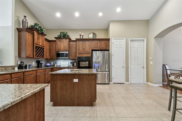 kitchen featuring light stone countertops, backsplash, stainless steel appliances, light tile patterned floors, and a center island