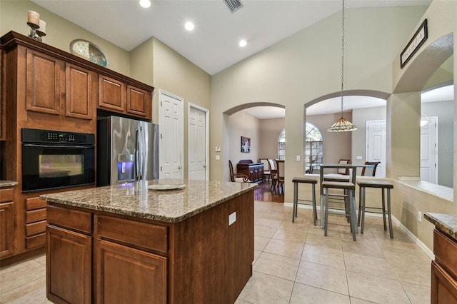 kitchen featuring pendant lighting, stainless steel fridge, light stone countertops, black oven, and a kitchen island