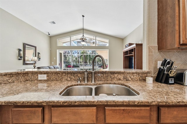 kitchen with light stone countertops, tasteful backsplash, vaulted ceiling, ceiling fan, and sink