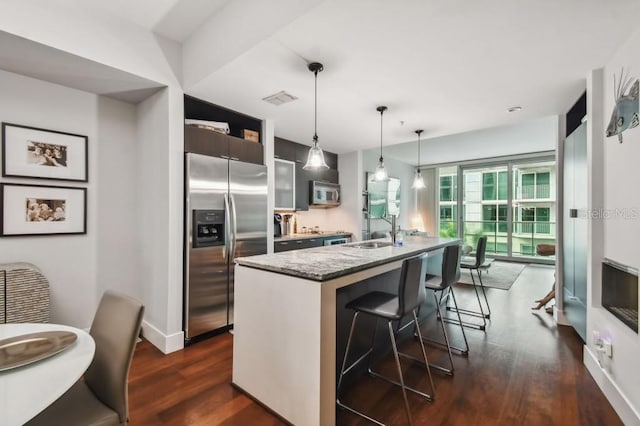 kitchen featuring hanging light fixtures, stainless steel appliances, dark hardwood / wood-style flooring, an island with sink, and a breakfast bar area