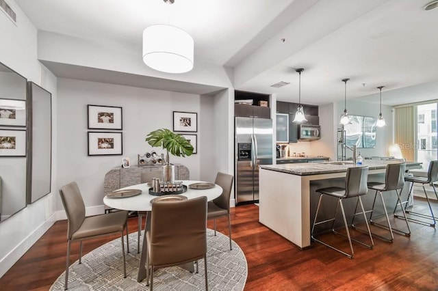 kitchen with dark hardwood / wood-style flooring, stainless steel appliances, a kitchen island with sink, decorative light fixtures, and a breakfast bar area