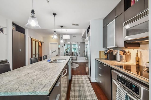 kitchen featuring sink, hanging light fixtures, stainless steel appliances, dark hardwood / wood-style floors, and a center island with sink