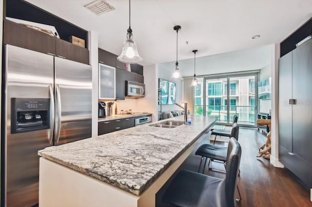 kitchen featuring pendant lighting, a center island with sink, sink, light stone counters, and stainless steel appliances