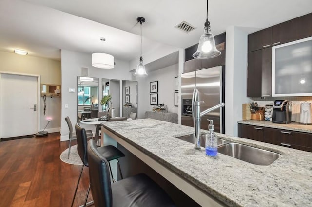 kitchen featuring high end refrigerator, dark brown cabinetry, decorative light fixtures, and light stone counters