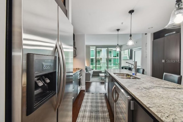 kitchen featuring decorative light fixtures, stainless steel appliances, light stone counters, and sink