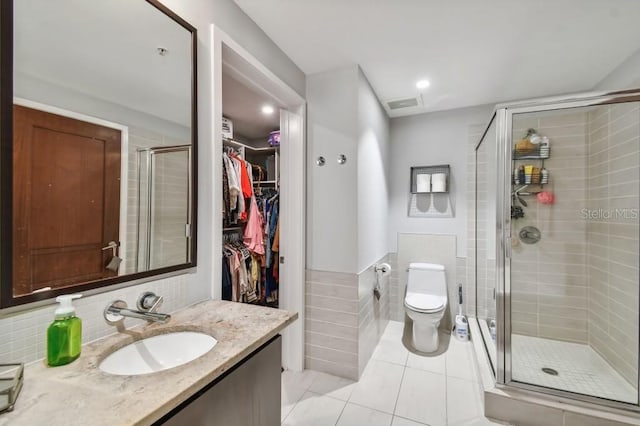 bathroom with tile patterned floors, toilet, a shower with door, vanity, and tile walls