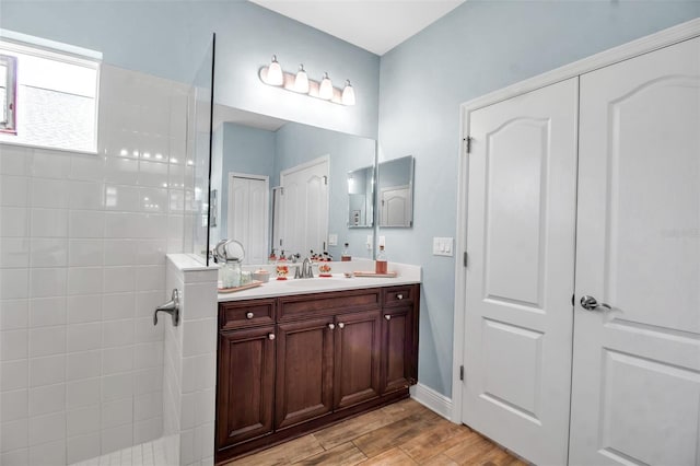 bathroom with hardwood / wood-style flooring, vanity, and tiled shower