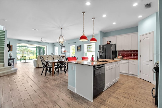 kitchen featuring a center island with sink, black dishwasher, pendant lighting, light stone countertops, and white cabinets