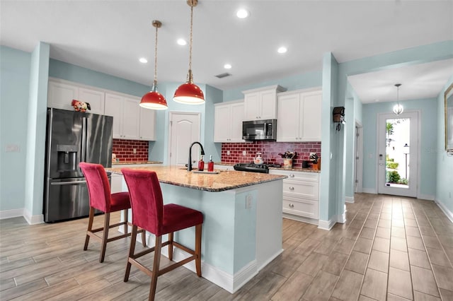 kitchen with white cabinetry, stainless steel appliances, a kitchen island with sink, and hanging light fixtures