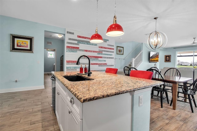 kitchen with sink, white cabinetry, hanging light fixtures, an island with sink, and light stone countertops