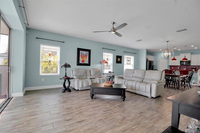 living room with ceiling fan with notable chandelier and a wealth of natural light