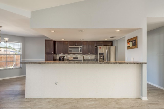 kitchen featuring appliances with stainless steel finishes, tasteful backsplash, dark brown cabinetry, a notable chandelier, and stone counters