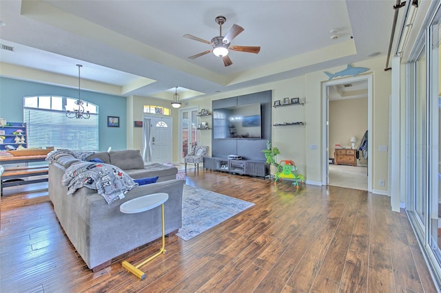 living room with hardwood / wood-style floors, ceiling fan with notable chandelier, and a raised ceiling