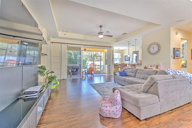 living room with a raised ceiling, ceiling fan, and dark wood-type flooring