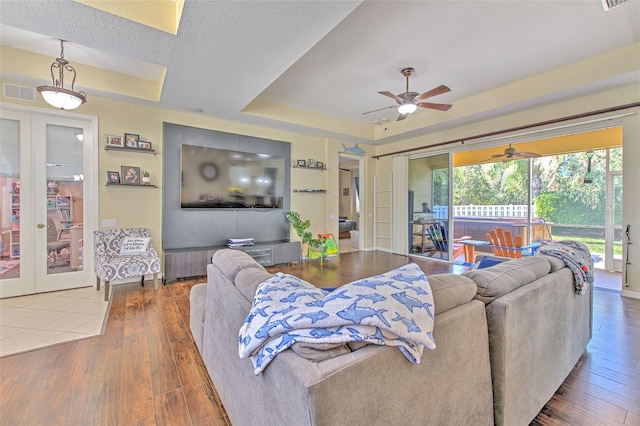 living room with french doors, a textured ceiling, a raised ceiling, ceiling fan, and hardwood / wood-style floors