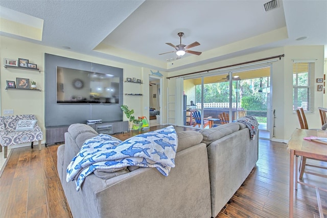 living room with ceiling fan, dark hardwood / wood-style flooring, and a raised ceiling