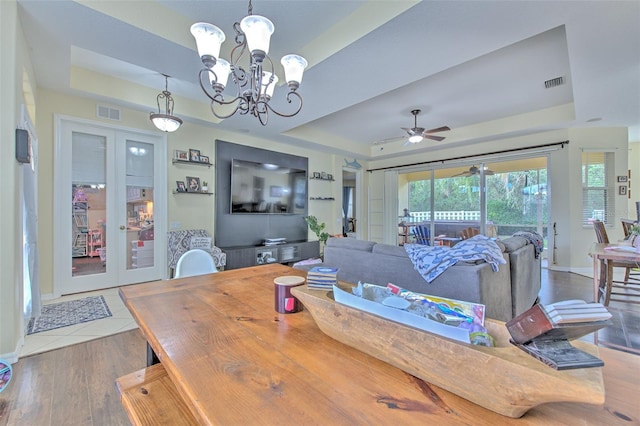 dining space featuring ceiling fan with notable chandelier, a raised ceiling, wood-type flooring, and french doors