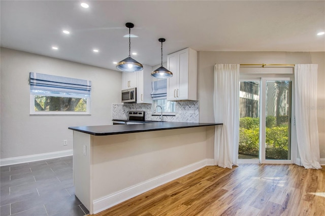 kitchen with kitchen peninsula, decorative backsplash, appliances with stainless steel finishes, decorative light fixtures, and white cabinetry