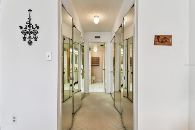 corridor featuring a textured ceiling and light colored carpet