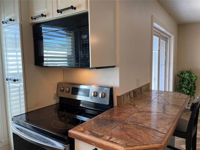 kitchen featuring electric range, white cabinetry, and tile countertops