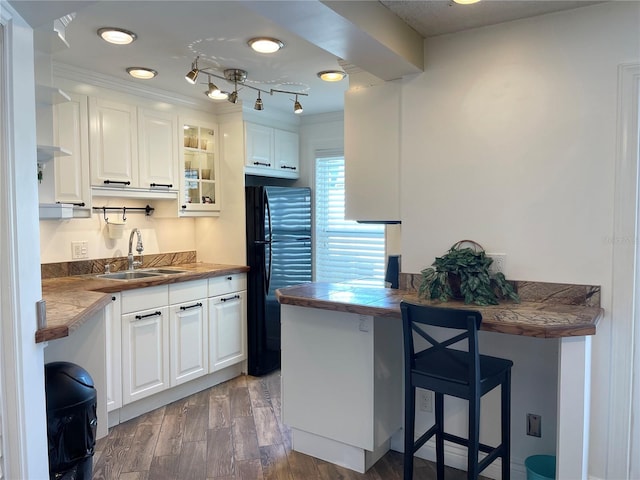 kitchen with kitchen peninsula, black fridge, sink, dark hardwood / wood-style floors, and white cabinetry